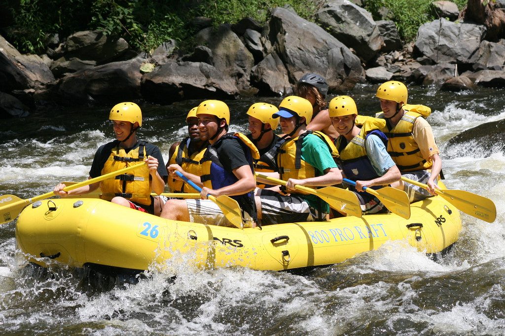 Yellow raft carrying eight helmeted, life-jacketed white water rafters in a choppy river